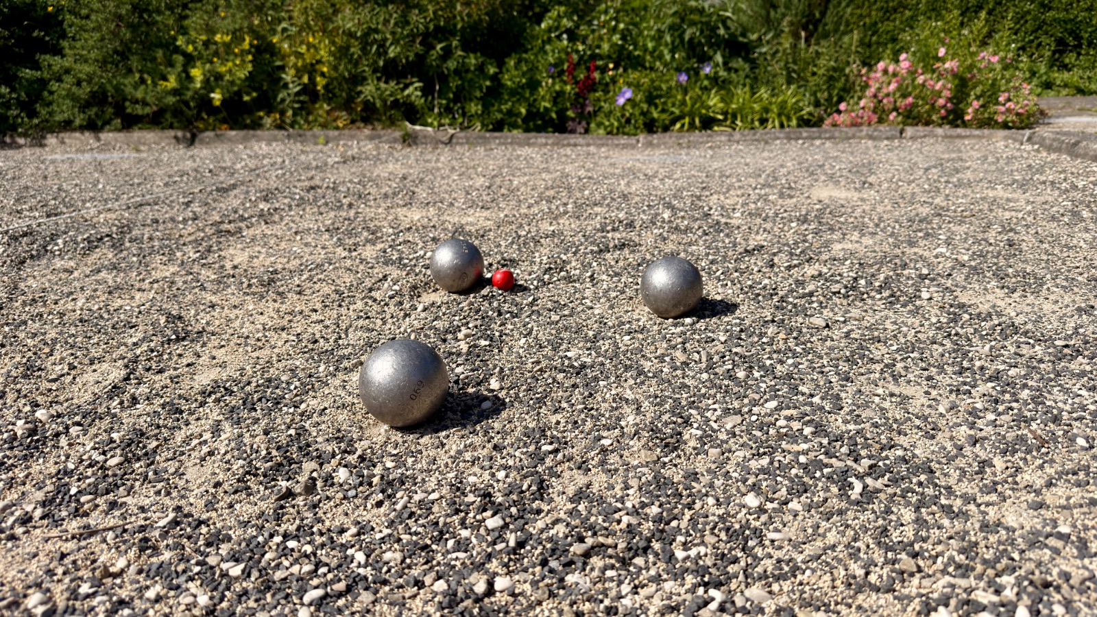 Three boules and the jack on a jeu de boules lane, framed by greenery